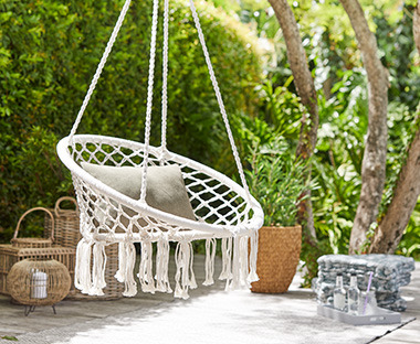 Підвісне крісло з легкого білого плетіння під деревом у саду