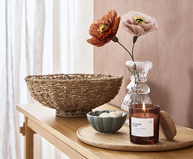 Скляна ваза зі штучними паперовими квітами та ароматичними свічками на дерев'яному підносі