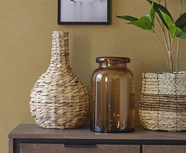 Плетена ваза та ваза з коричневого скла на комоді