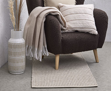 Крісло з декоративними подушками та пледом і килимом на підлозі