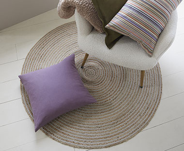 Круглий килим на підлозі з фіолетовою декоративною подушкою, що лежить зверху