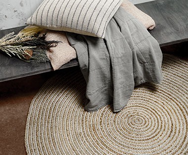 Світлий круглий плетений килим біля сірий плед та подушка