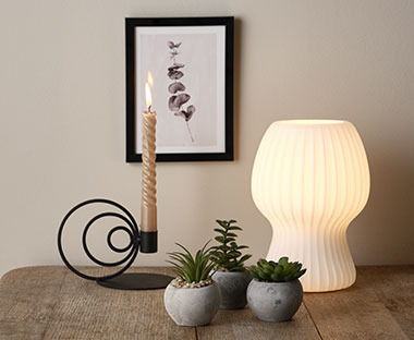 Настільна лампа, свічник зі свічкою та три маленькі декоративні горщики зі штучними рослинами