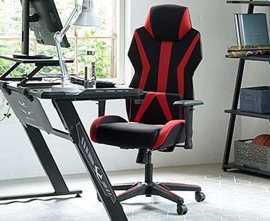 Крісло геймерське чорно - червоного кольору на коліщатах біля чорного столу