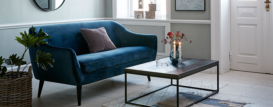 Синій оксамитовий диван поруч з кавовим коричневим столиком у вітальні