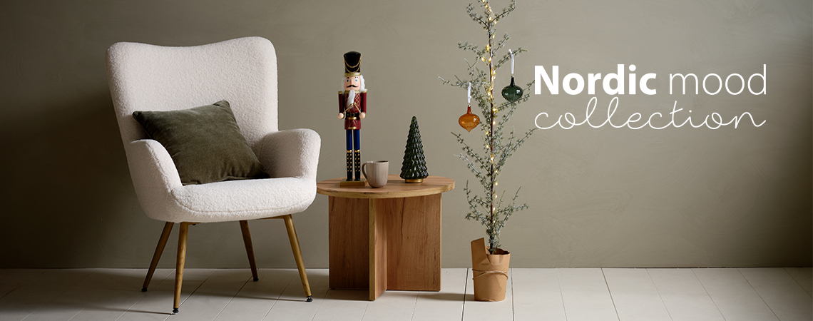 Крісло з подушкою, кавовий столик із різдвяною фігуркою та витончена ялинка, прикрашена скляними прикрасами.