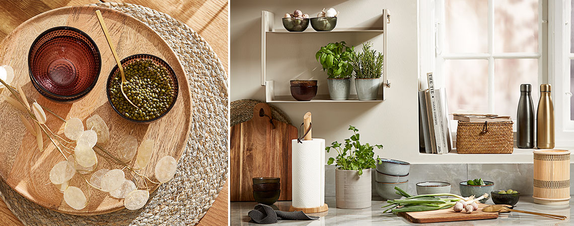 Скляні миски на плетеному килимку та керамічні кухлі зі свіжою зеленню на настінній полиці на кухні