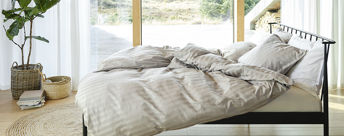 Спальня з чорним металевим ліжком, ковдрами та подушками, в смугастій постільній білизні світло-сірого та білого кольору