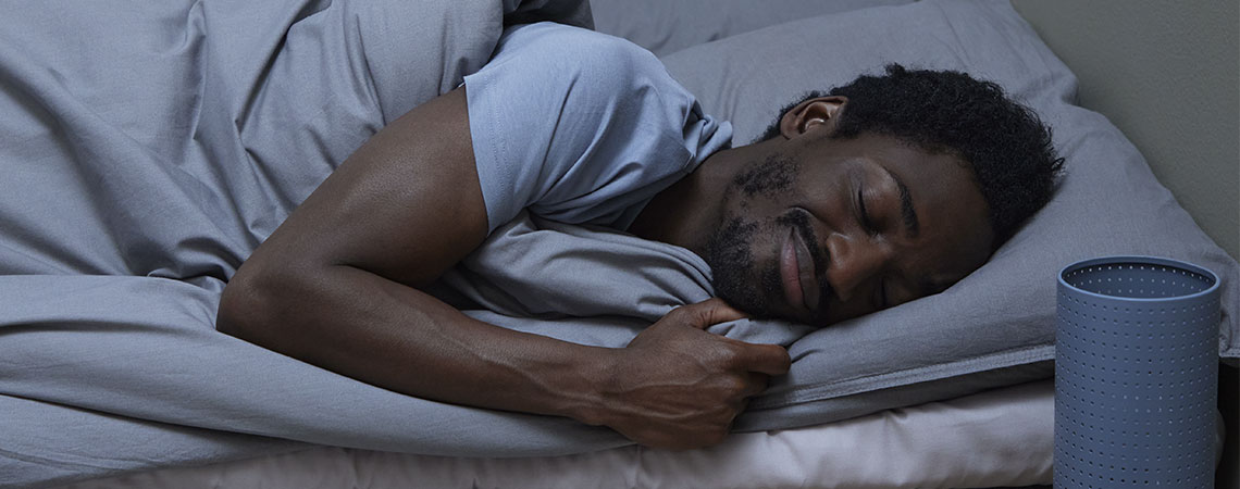 Чоловік спить у ліжку з сірою подушкою та ковдрою