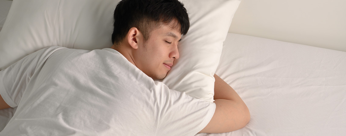 Чоловік відпочиває в ліжку з білою подушкою та білим наматрацником