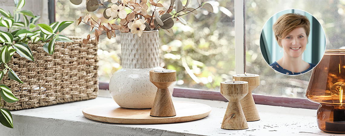 Підвіконня з лампою, дерев'яні свічники, біла рельєфна ваза та кошик з рослиною
