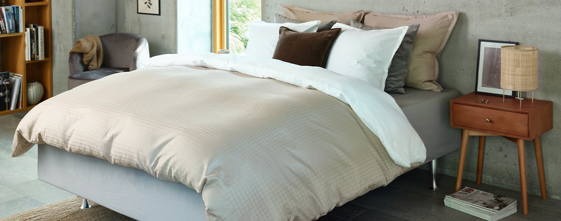 Ліжко застелене сатиновою постільною білизною бежевого кольору і багато подушок різних розмірів на ліжку