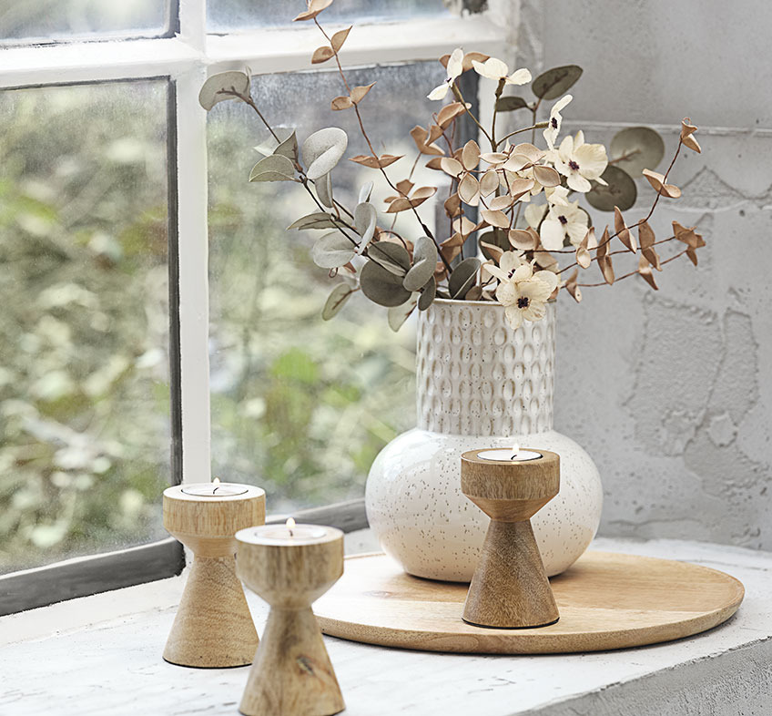 Світло-бежева ваза з тисненням та штучними квітами і дерев'яними свічниками