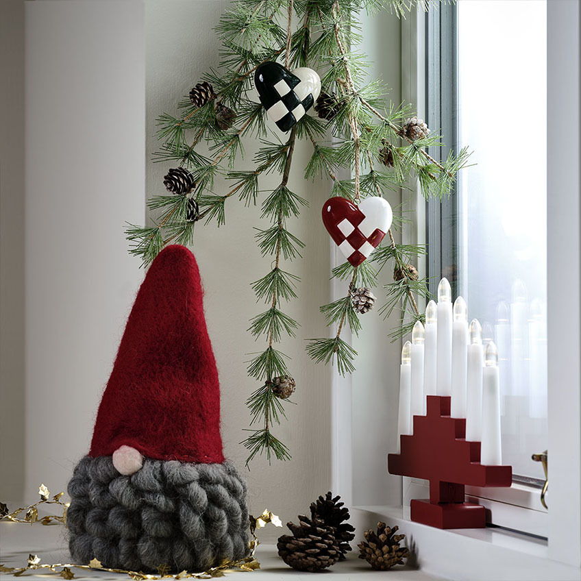 Різдвяний гном у червоному капелюсі та з сивою бородою, різдвяні прикраси у вигляді серця та червона арка з свічок білого кольору.