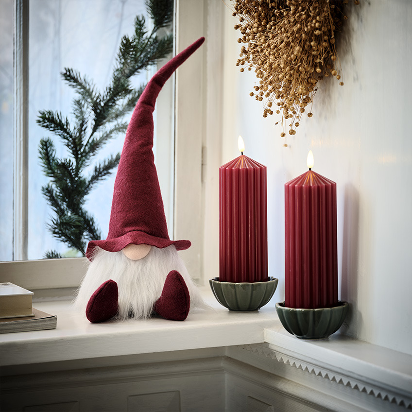Скандинавський різдвяний ельф на підвіконні поруч з великими червоними свічками  