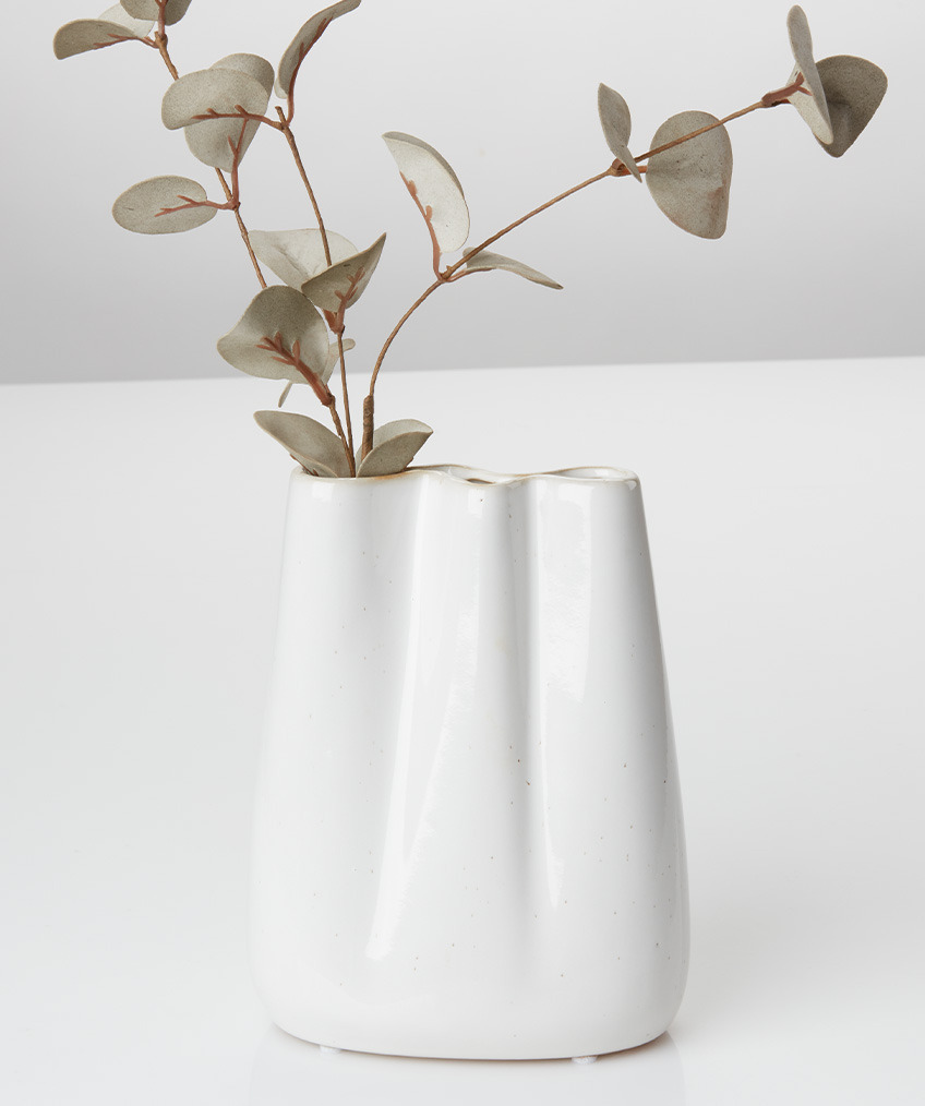 Біла ваза з плавними контурами, хвилястими краями та штучною гілочкою