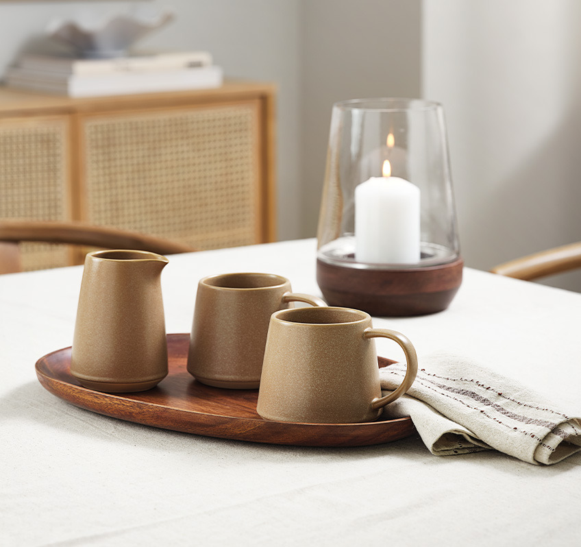 Керамічний кухоль і молочник коричневого кольору на обідньому столі з тканинною серветкою і скатертиною 