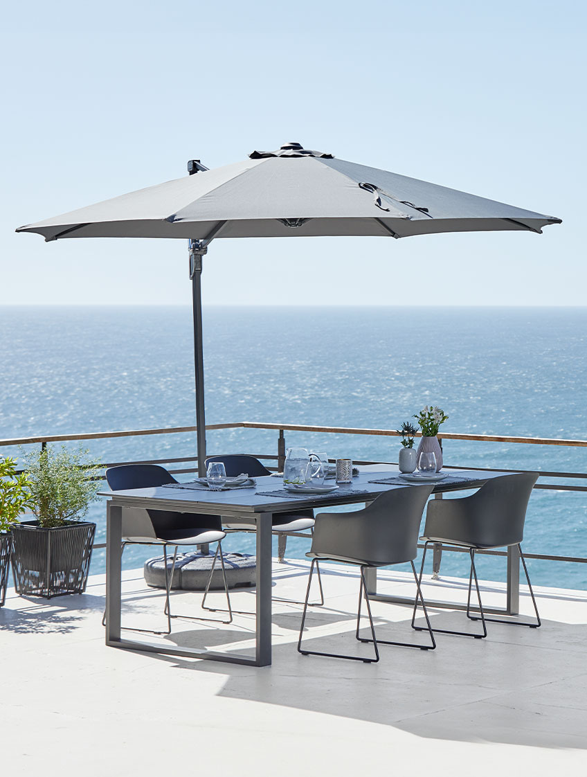 Велика підвісна парасоля, садовий стіл та стільці на патіо біля моря