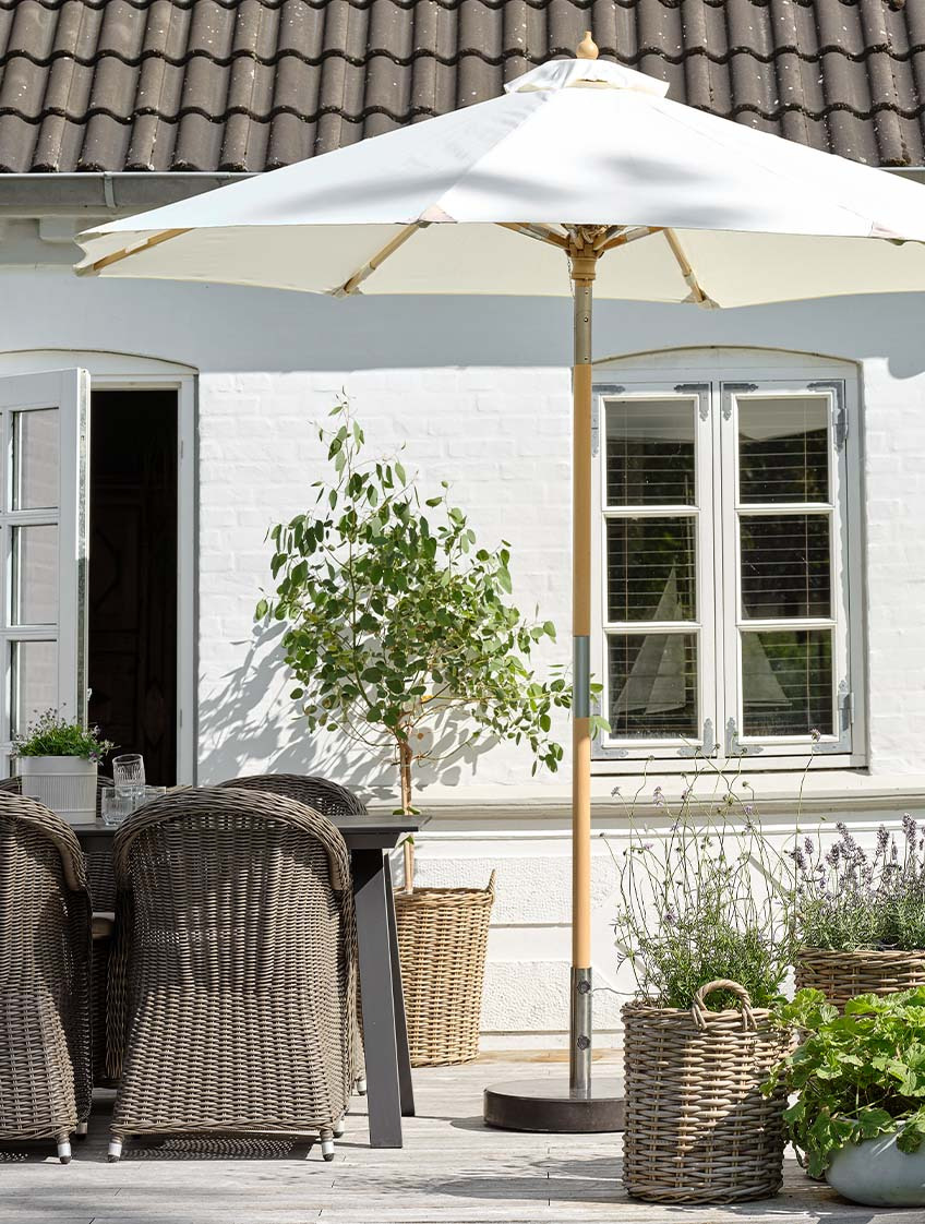 Класична садова парасоля лляного кольору на патіо з садовим столом та садовими стільцями  