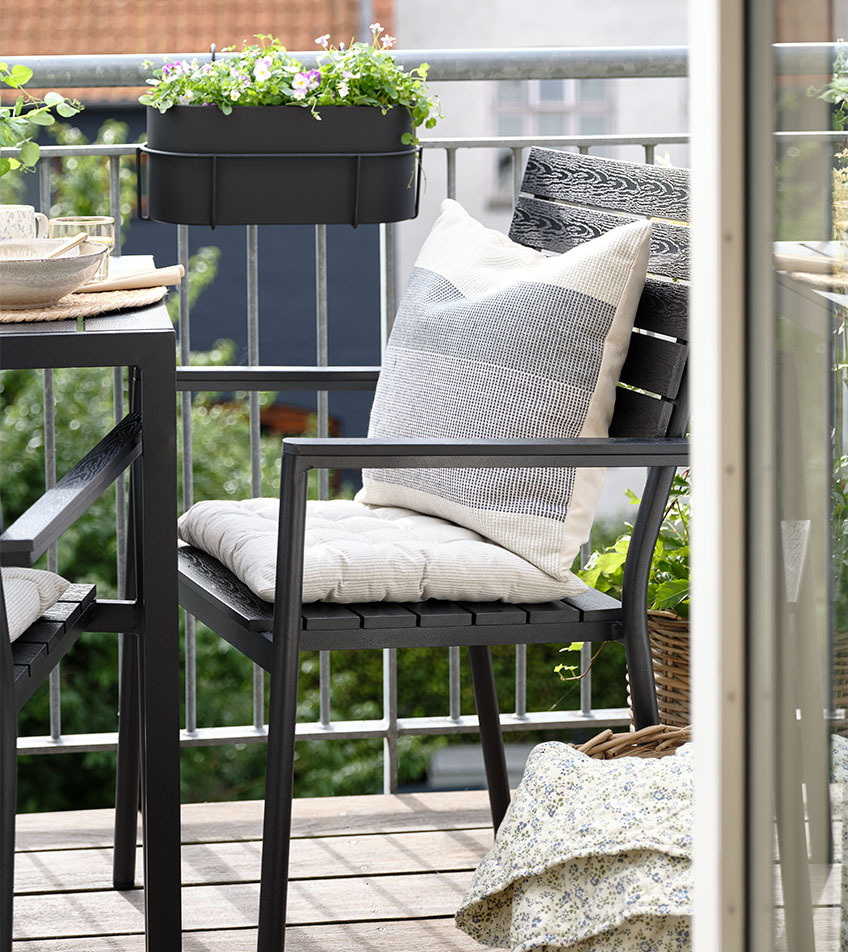 Чорний садовий стілець, який можна зберігати стопкою, з подушками на балконі