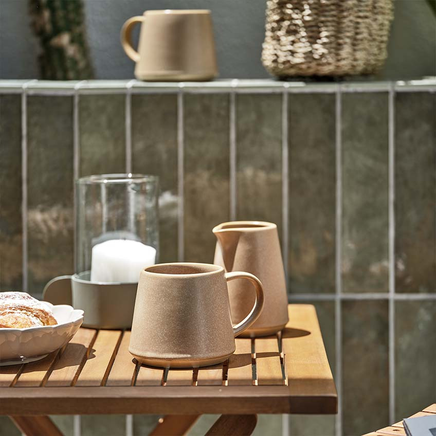 Горнятко кави та молочник на маленькому дерев'яному садовому столику на яскравому сонці 