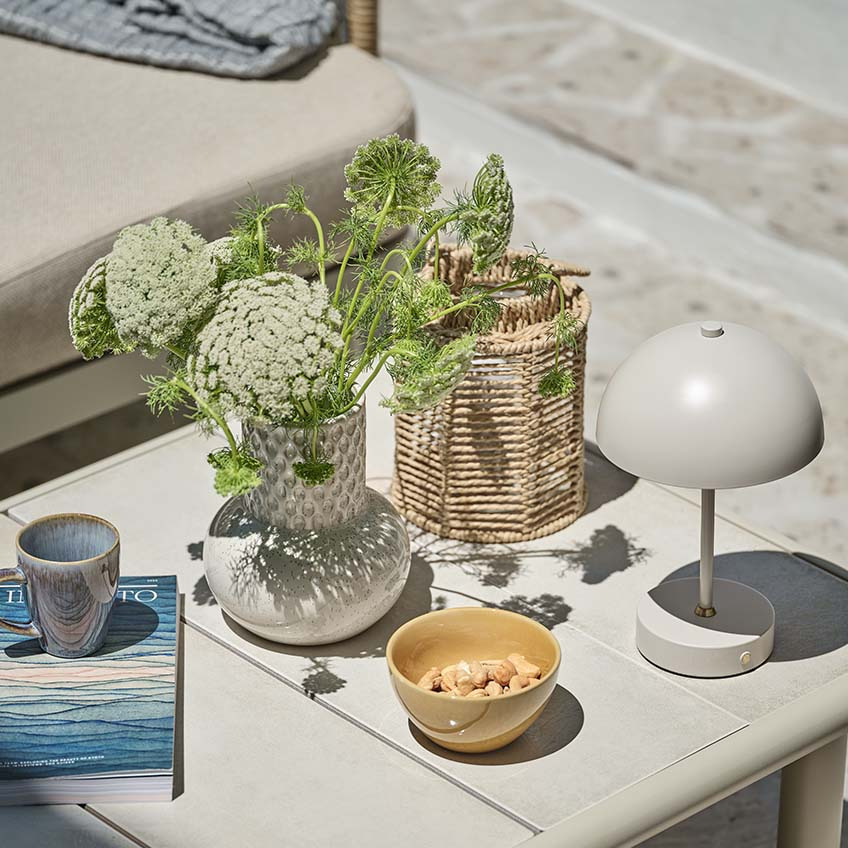 Невеликий садовий столик з різноманітним декором, включаючи невелику лампу на батарейках, вазу та ліхтар