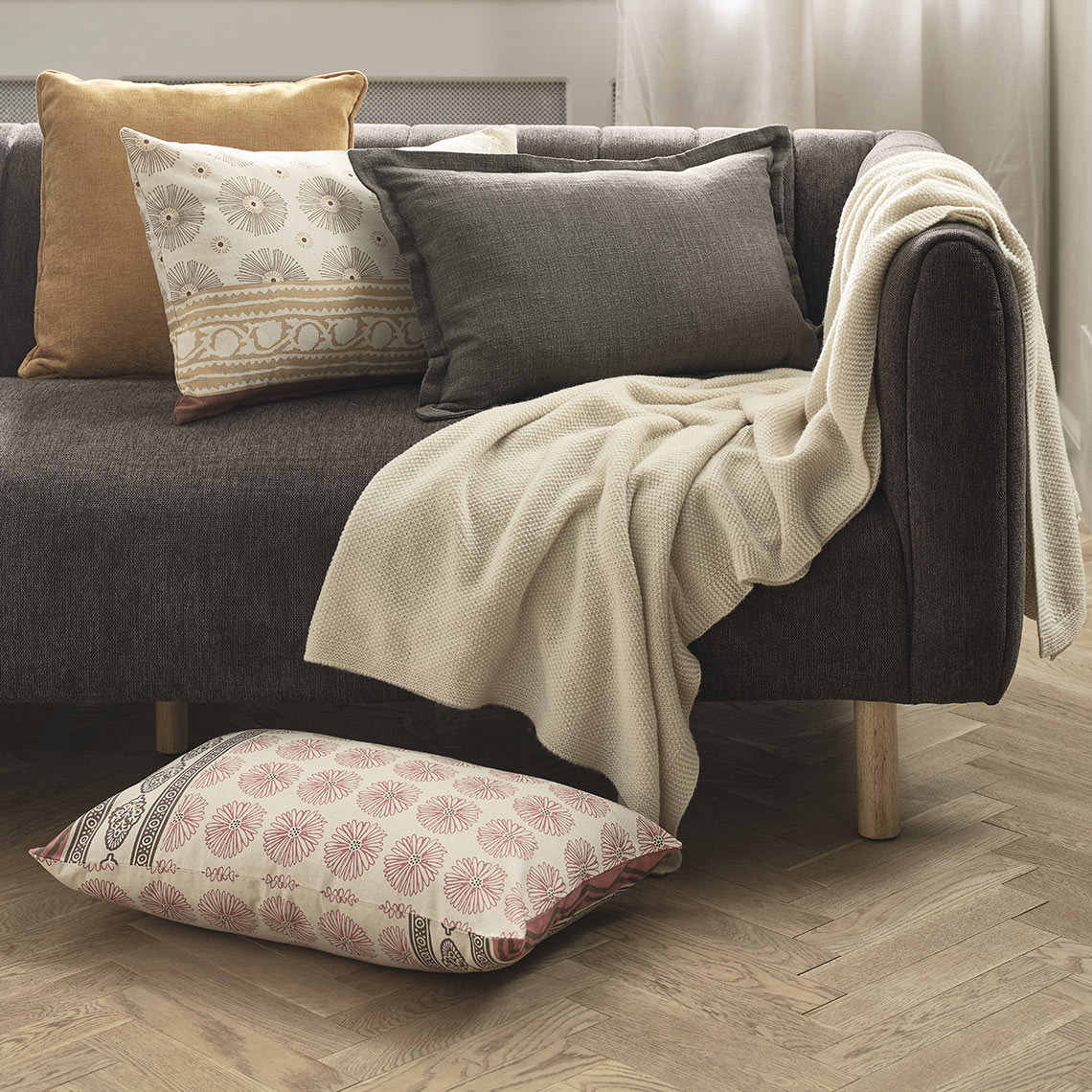 Декоративні подушки у стишених бежевих та роежвих кольорах зі світлим пледом на сірому дивані