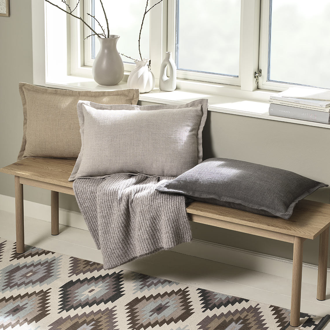 Декоративні подушки у чохлах коричневих відтінків та дерев'яній банкетці