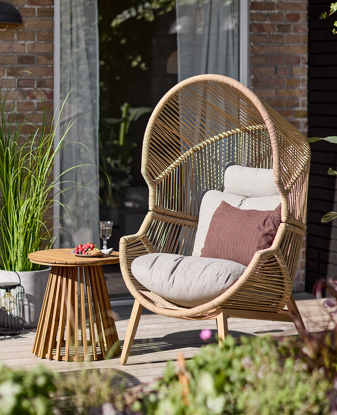 Плетене лаунж-крісло натурального кольору з м'якими подушками на терасі біля дерев'яного столика