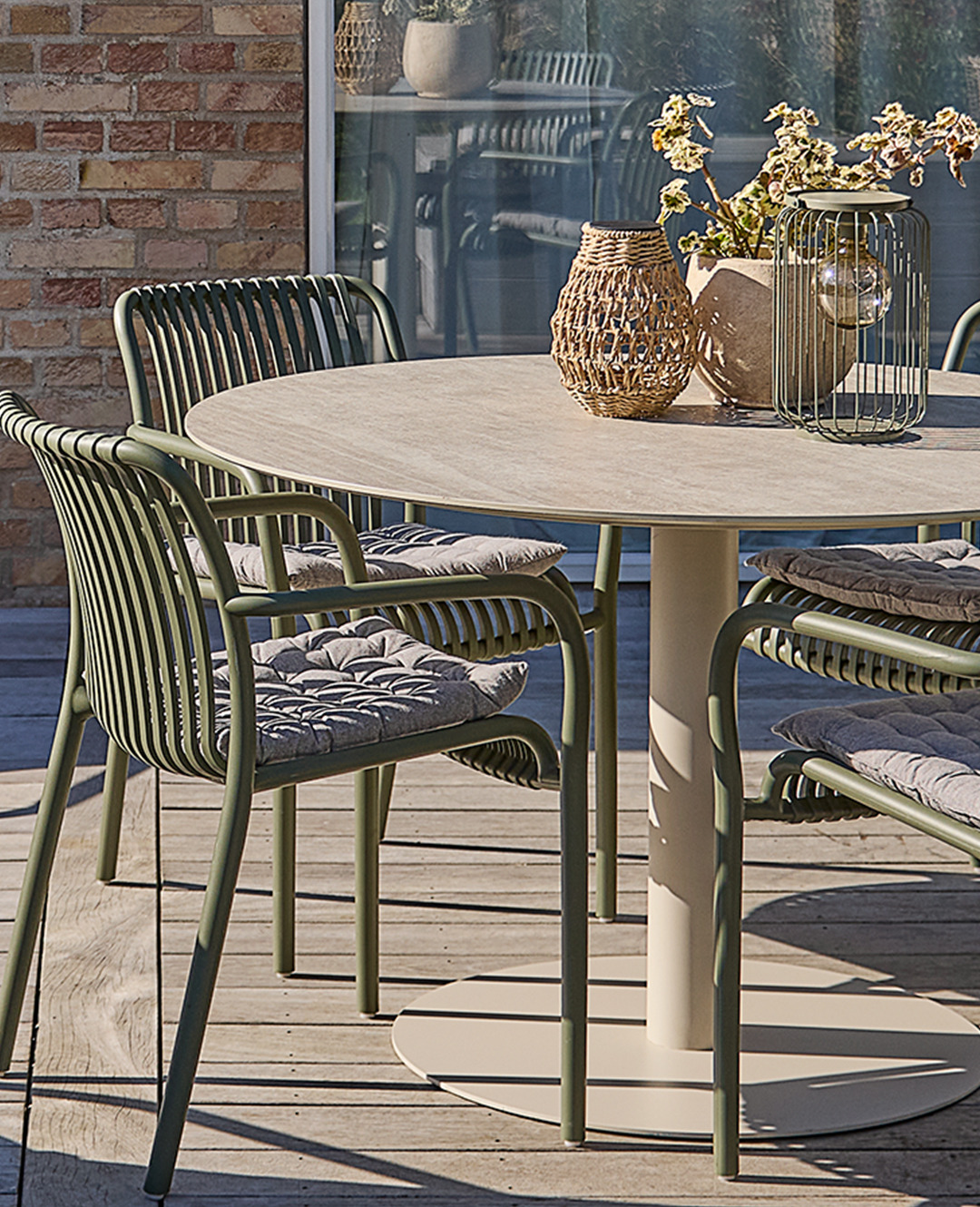 Садовий круглий стіл бежевого кольору з декором біля садових зелених металевих стільців на терасі