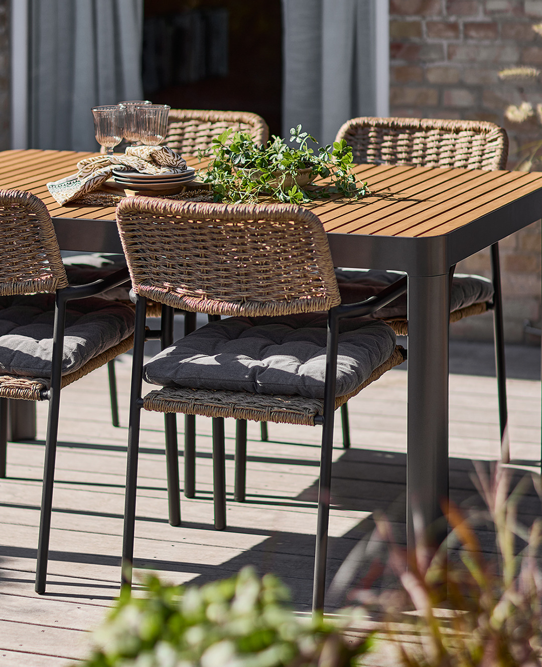 Стіл садовий з хардвуду поруч з плетеними садовими стільцями на сонячній терасі 