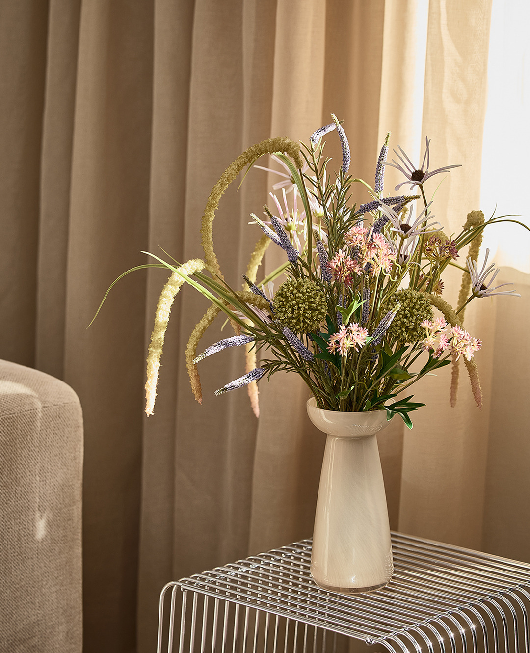 Висока бежева ваза з букетом на металевій підставці біля дивану