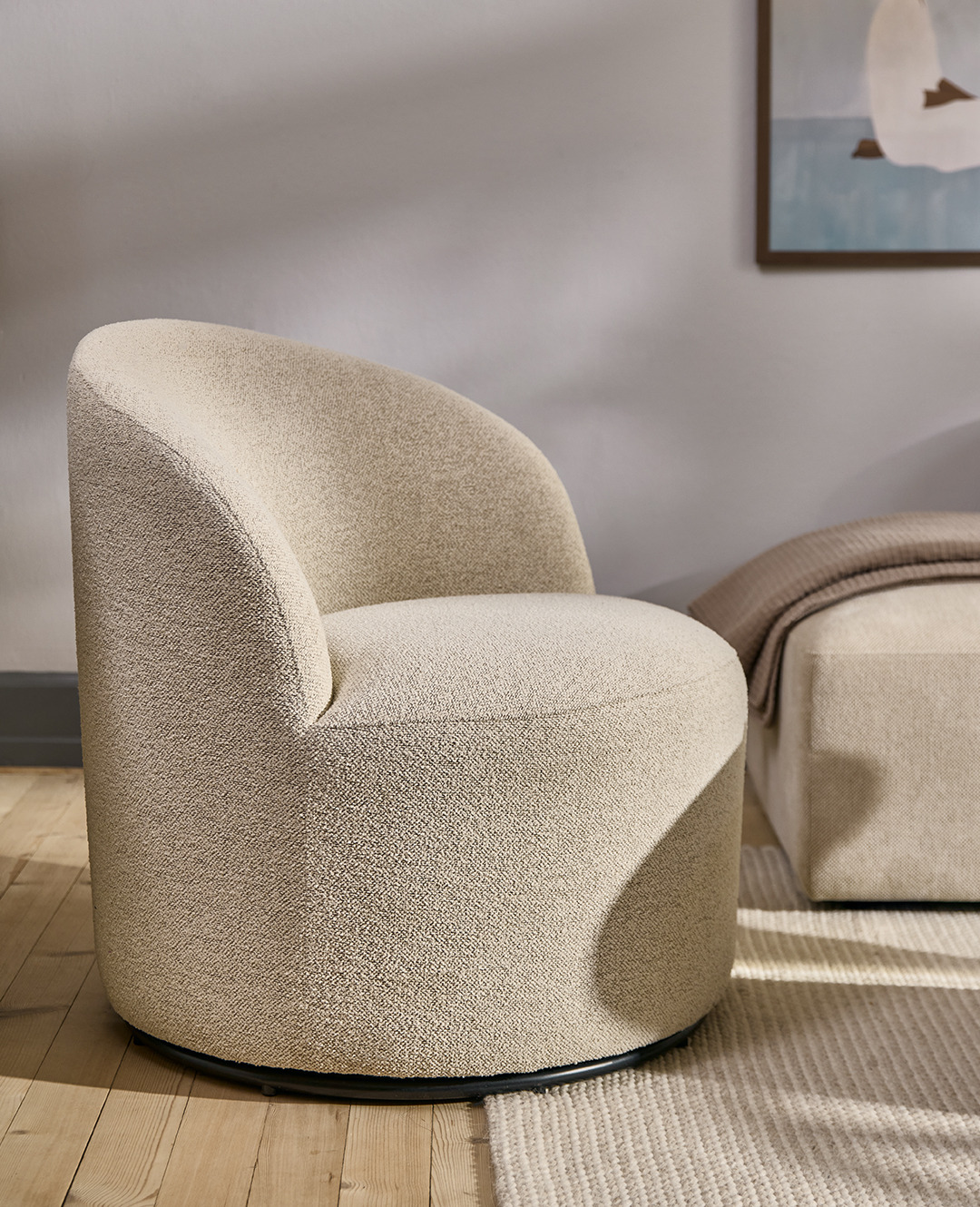 Обертальне лаунж крісло з м'якою бежевою оббивкою у вітальні поруч з диваном та килимом в бежевих відтінках