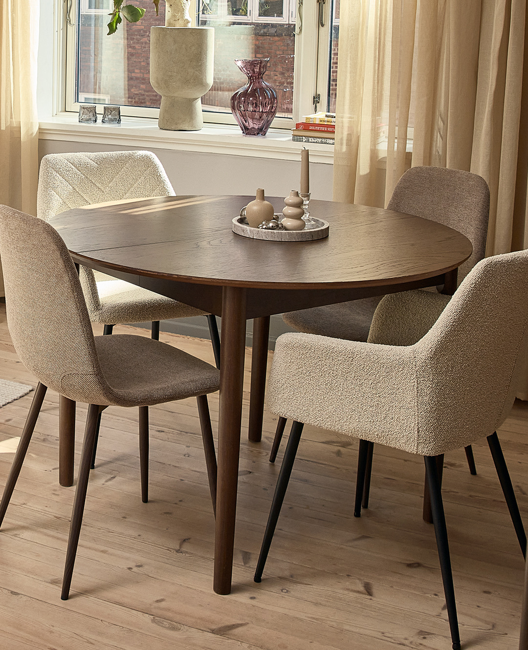 Круглий коричневий обідній стіл біля вікна та різні кухонні стільці бежевих відтінків