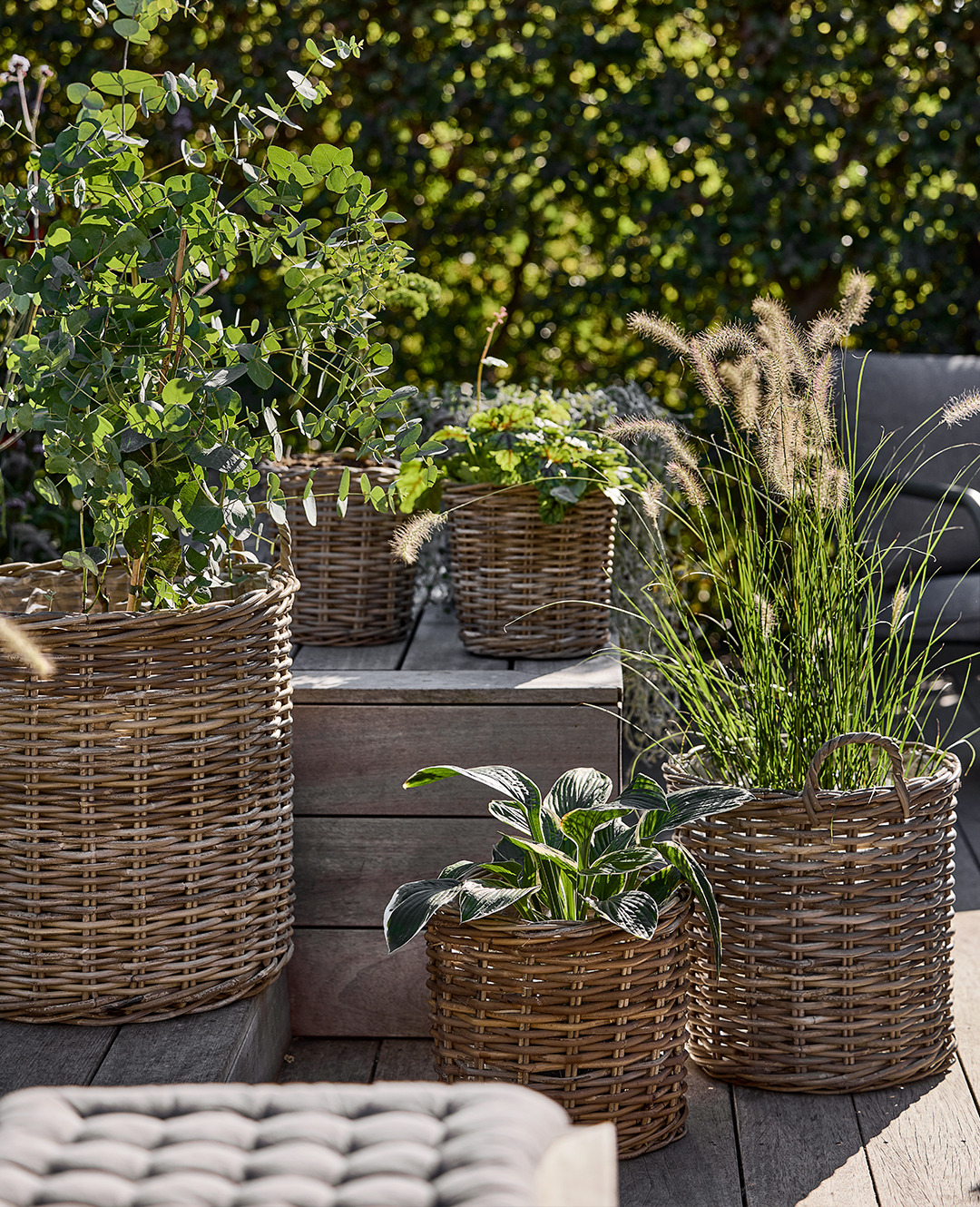 Плетені кошики натурального коричневого кольору різного розміру з квітами та росланами на терасі