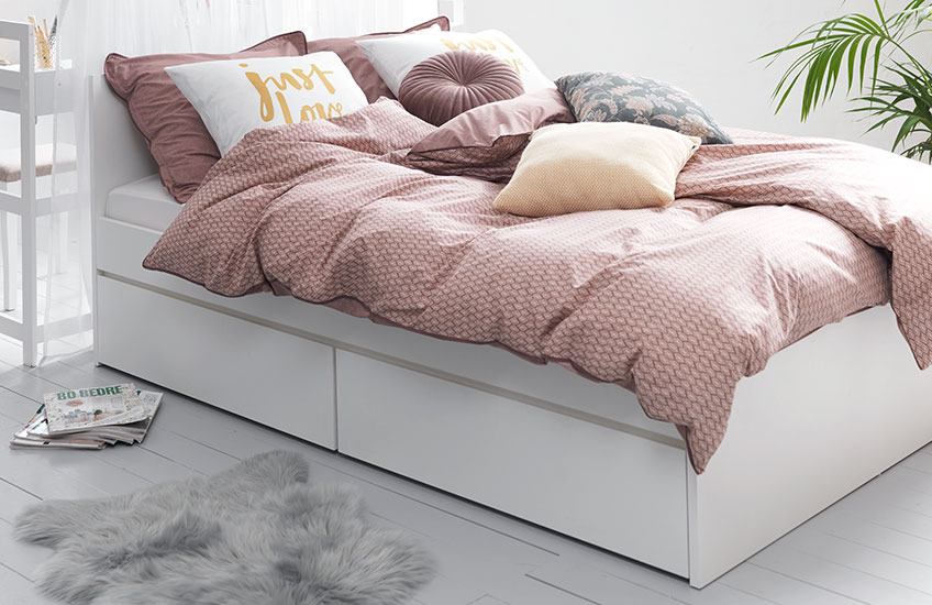 Біле ліжко з висувним коробом, застелене рожевою постільною білизною