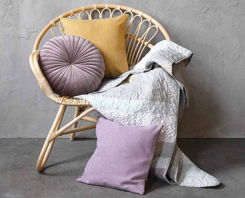 Плетене крісло з декоративними подушками та зі стьобаним пледом