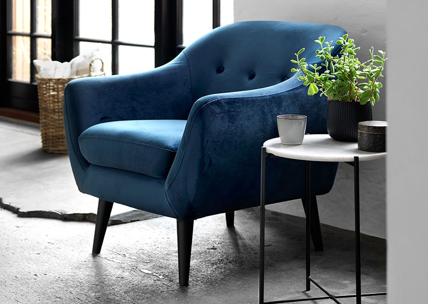 A living room with a blue velvet armchair and a coffee table 