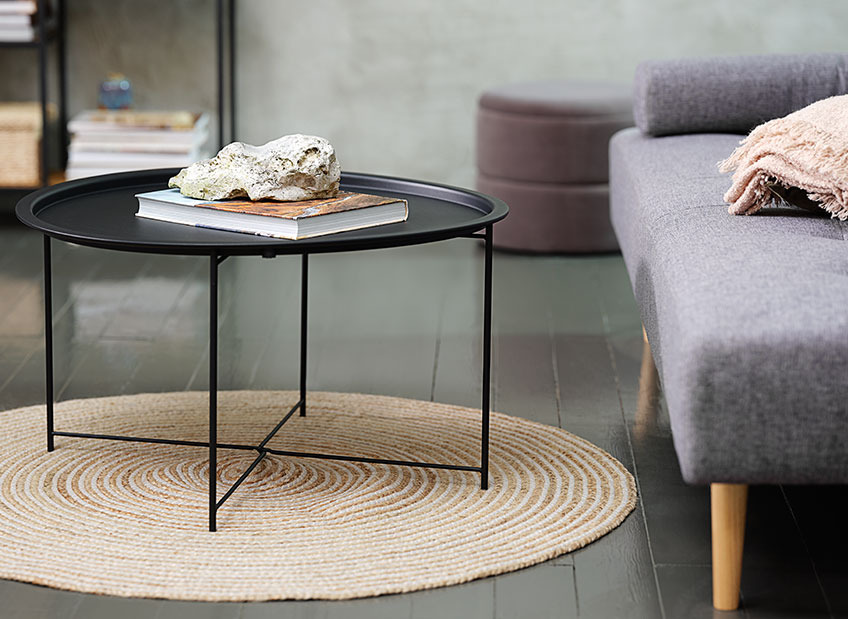 Чорний круглик столик на плетеному круглому килимі біля софи