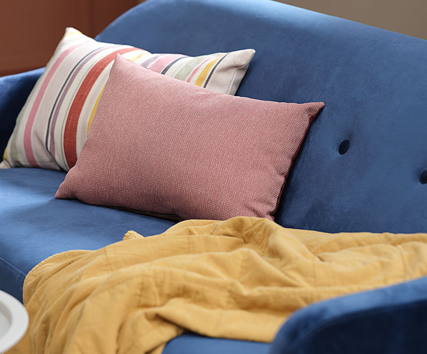 Кольорові подушки та жовтогарячий плед на синьому дивані