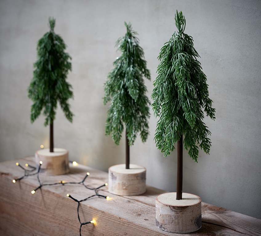 Three artificial pine trees on a log represent modern Christmas décor
