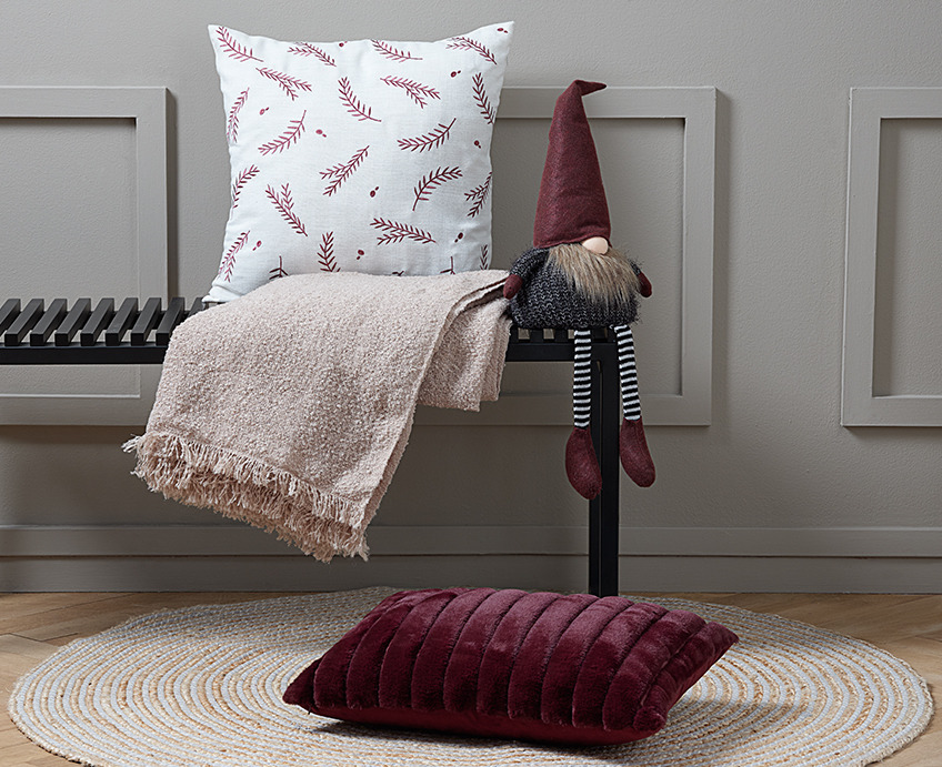Bench with a cushion, a throw and an elf. On the floor in front of the bench, a red cushion on a round rug.