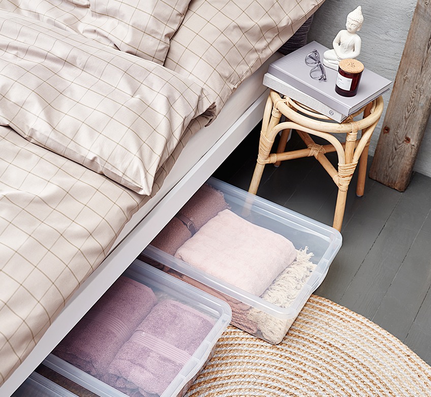 Ліжко з картатою постільною білизною, табурет та пластикові короби з речами