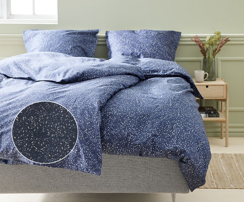 Ліжко з блакитною постільною білизною з листяним принтом в спальні з тумбочкою і настільною лампою