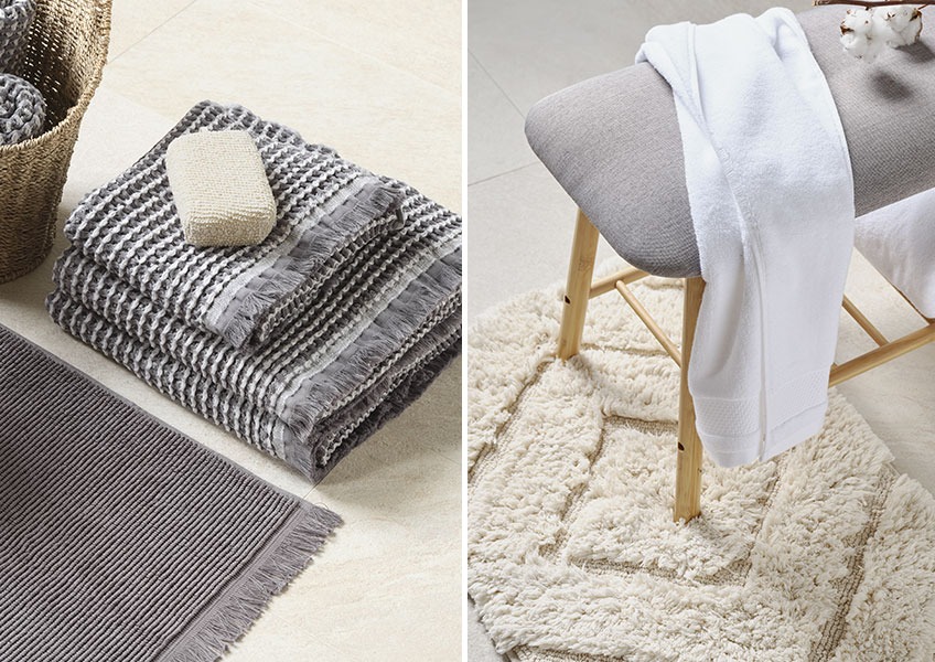Сірі вафельні рушники та білий рушник на лавці на білому килимку для ванни