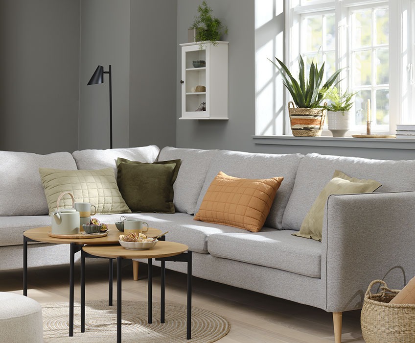 Вітальня облаштована сірим диваном і помаранчевими, зеленими та бежевими подушками