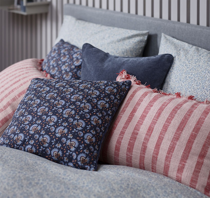 Ліжко з декоративними подушками у червоних та синіх тонах.