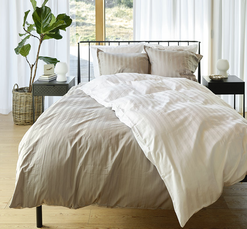 Спальня з сіро-білою смугастою постільною білизною на ліжку та двома тумбочками