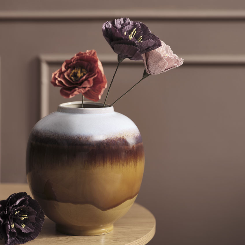 Різнокольорова ваза на столі зі штучними квітами червоного, фіолетового та рожевого кольорів