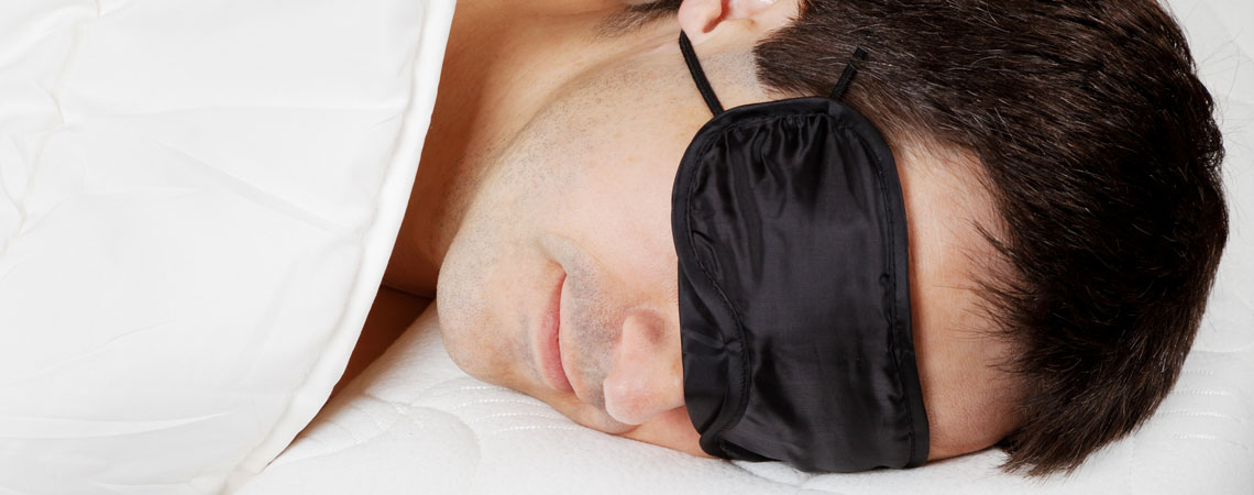 Чолокі спить у масці для сну на ліжку з білою постільною білизною